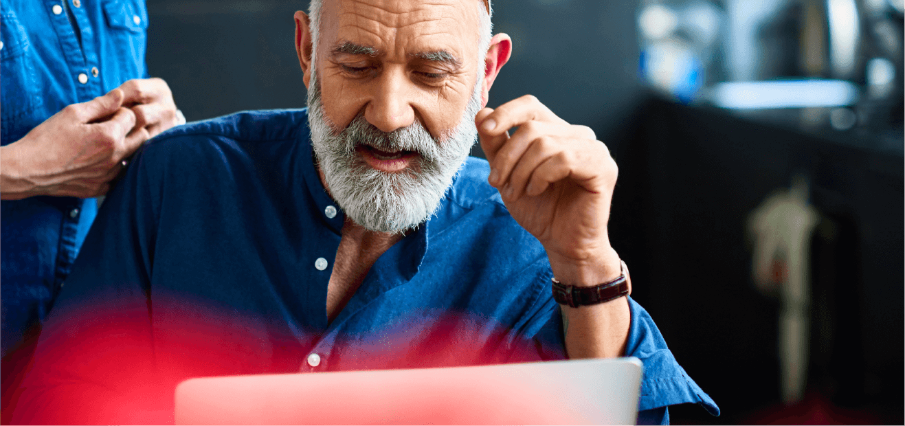 Person in a denim shirt working on a laptop with another person standing behind