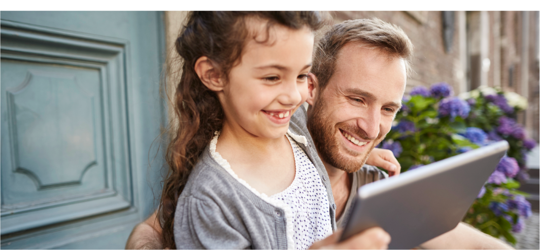 Young girl holding a tablet device smiling with her dad with purple flower backdrop
