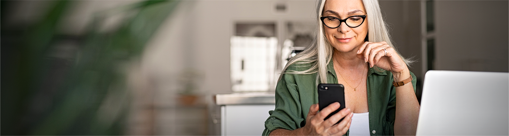 Woman with grey hair and green shirt sitting looking at her phone.