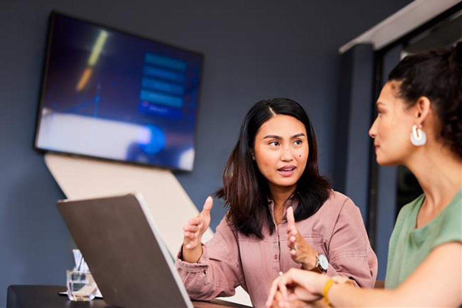 Two women engage in conversation, with one gesturing animatedly, showing interest and involvement in the discussion