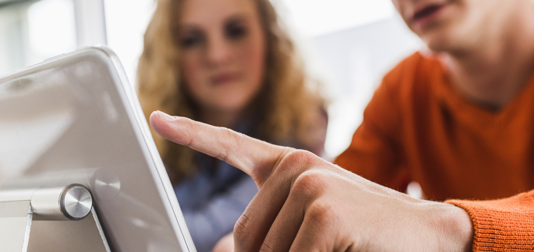 Close up image of man pointing at a computer screen with a woman sitting next to him looking at the screen.