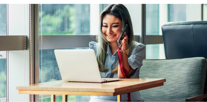 Woman happily talking on phone while sitting in front of laptop.